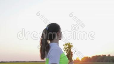 一个年轻的女人带着一束来自<strong>菜籽油</strong>的鲜花在夕阳下散步